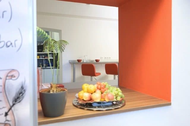 Durchreiche zum Aufenthaltsraum mit Obstschale vor oranger Wand