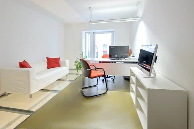 Besprechungszimmer mit heller Sitzbank, Schreibtisch und rotem Stuhl