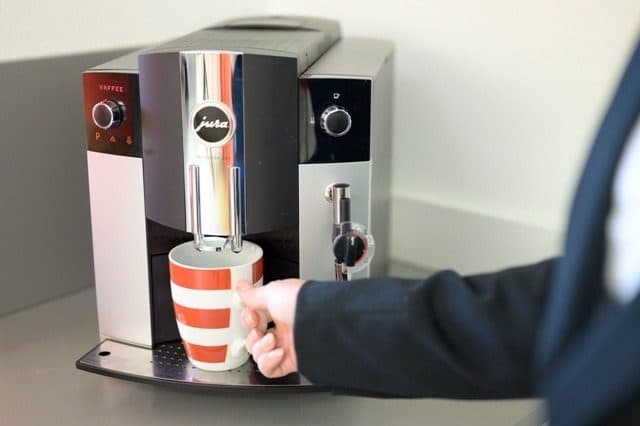 Kaffeeautomat, eine Hand stellt eine gestreifte Tasse darunter
