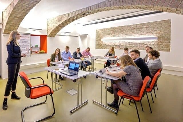 Trainerin geht durch den Raum, Teilnehmende arbeiten am Laptop