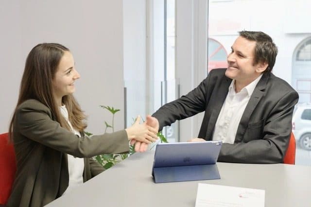 Beraterin und Kunde geben sich am Besprechungstisch die Hand