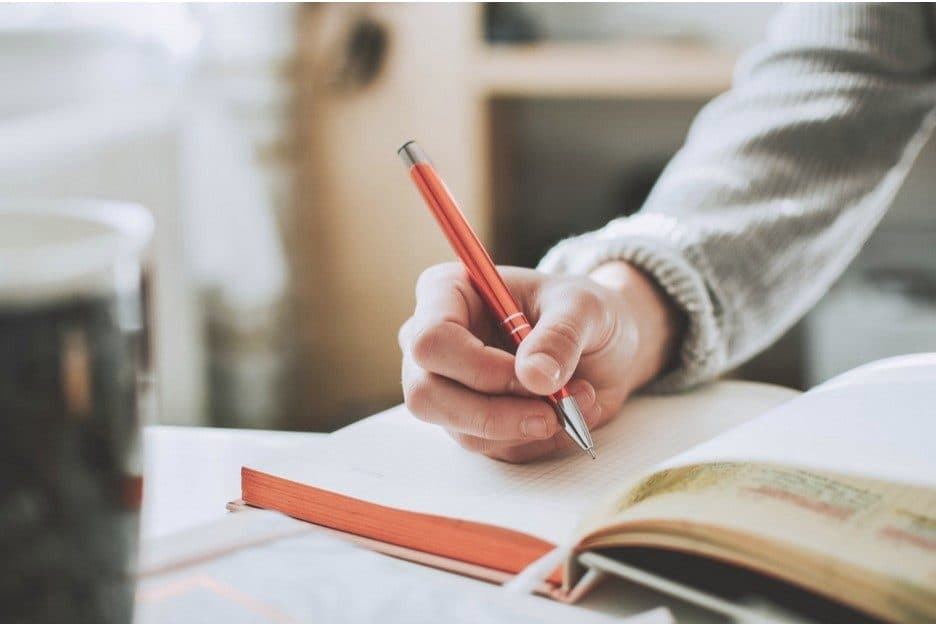 Hand schreibt mit einem roten Stift Notizen in ein aufgeschlagenes Buch
